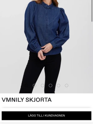 Blå denimskjorta från Vero Moda - Trendig blå skjorta i denim från Vero Moda med klassisk krage och långa puffärmar. Skjortan har knappar framtill som döljs av en slejf och är tillverkad i bomull. Perfekt för en cool och avslappnad look.