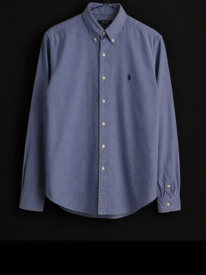 Blå skjorta från Ralph Lauren - Klassisk blå skjorta från Polo Ralph Lauren i slim fit-modell. Skjortan har knappar framtill, button-down krage och den ikoniska broderade loggan på bröstet. Tillverkad i bomull och har långa ärmar med manschettknappar.