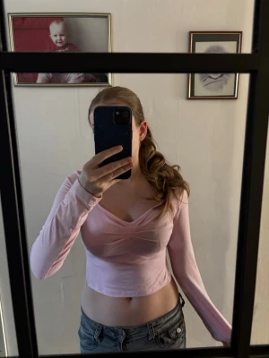 Ljusrosa croppad långärmad topp - Säljer en ljusrosa croppad topp med lång ärm och v-ringad hals. Toppen har en figurnära passform och är tillverkad i ett mjukt, stretchigt material. Perfekt att styla med jeans eller kjol för en trendig look.