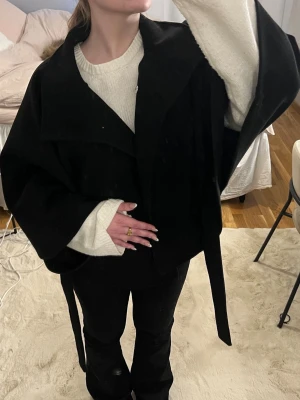 Populär svart kappa med knytskärp - Stilren svart kappa med bred krage och knytskärp i midjan. Bara provad