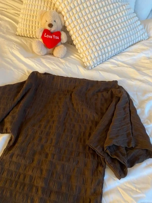 Brun klänning från Nelly i XS - Brun topp från Nelly i storlek XS. Toppen har loose passform och är gjord i ett strukturerat, krinklat tyg som ger en modern känsla. Perfekt för dig som gillar en avslappnad och trendig stil.