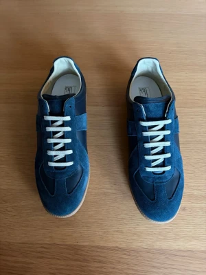 Blå sneakers i mocka och läder - Snygga sneakers i blå mocka och mörkblått läder med vita snören och beige sula. Klassisk retrodesign med låg profil och rundad tå. Perfekta för dig som gillar stilrena och tidlösa sneakers med en sportig vibe.