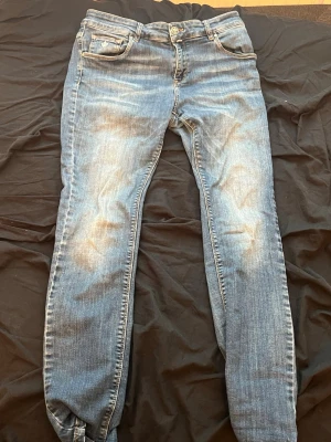 Blå jeans med broderad detalj - Snygga blå Morris jeans med slitningar och en broderad lilja på myntfickan. Klassisk femficksmodell med orange kontrastsömmar och smal passform. Perfekta för en avslappnad och trendig look.🚨 Nypris 1500🚨
