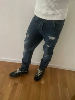 Mörkblå hammond slitna jeans  - Säljer ett par hammond mörkblå jeans med flera slitningar och hål på benen. Jeansen har en smal passform och klassisk femficksdesign. 