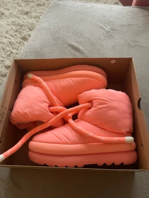 Neonrosa moon boots med tjock sula - Helt oanvända med kartong, Moon boots i neonrosa med kraftig, räfflad sula och breda matchande snören. Skorna har en puffig och vadderad design som ger en cool och modern look. Materialet är syntet och bootsen är riktigt eye-catching för dig som gillar att sticka ut.