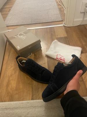 Mörk blåa sneakers från Christian Louboutin - Snygga svarta sneakers från Christian Louboutin i mocka med klassisk låg siluett och svarta snören. Skorna har en stilren design med diskret branding och svart sula. Perfekta för dig som gillar exklusiva och trendiga sneakers. Storlek 43 passar 42 obs box medföljer ej
