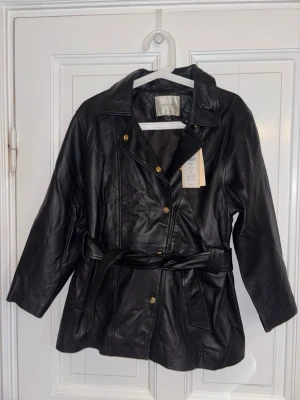 Selected Femme Äkta Skinnjacka – 100% Lammskinn – Strl 38 – Ny med tags - Exklusiv och tidlös skinnjacka från Selected Femme i mjukt äkta lammskinn. Elegant modell med guldfärgade detaljer, midjebälte och stilren passform som passar perfekt både till vardag och mer uppklädda outfits.  • Märke: Selected Femme • Modell: SFSONJA 7/8 Leather Jacket • Storlek: 38 • Färg: Svart • Material: 100% äkta lammskinn • Skick: Helt ny med tags kvar  