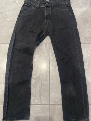 Svarta raka jeans  - Säljer ett par svarta jeans från Jack and Jones med rak passform och klassisk femficksdesign. Jeansen har normal midja och är tillverkade i denim med en lätt tvättad look. Perfekta för en avslappnad och stilren outfit.