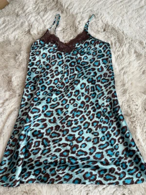 Leopardmönstrat nattlinne med spets - Snyggt nattlinne i satin med blått och brunt leopardmönster. Tunna justerbara axelband och brun spets vid bysten ger en extra touch. Perfekt för dig som gillar djurmönster och vill ha något mjukt och glansigt på natten.