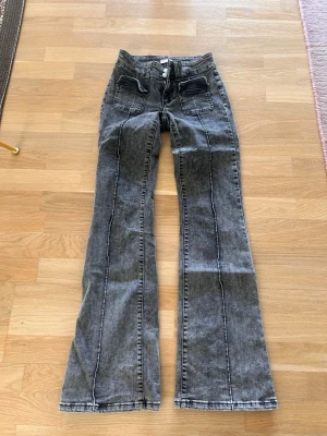 Grå utsvängda lågmidjade  jeans med fickor - Snygga grå lågmidjade jeans med utsvängda ben och markerade sömmar framtill. Jeansen har två stora fickor fram och två bak, samt knäppning med två knappar. Perfekta för en trendig och avslappnad look.