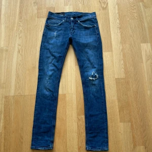 Blå jeans från Dondup med slitningar - Säljer ett par blå jeans från Dondup med snygga slitningar på låret och vid fickan. Klassisk femficksmodell med raka ben och normal passform. Ikonisk D-detalj på bakfickan. Perfekta för en avslappnad stil. Tveka inte att höra av er! Pris kan diskuteras!