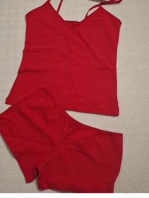 Rött linne och shorts set - Säljer ett rött underklädesset med linne och matchande shorts. Linnet har smala axelband och V-ringning, medan shortsen har en bekväm resår i midjan. Perfekt för att chilla hemma eller som sovplagg. Materialet känns mjukt och stretchigt.
