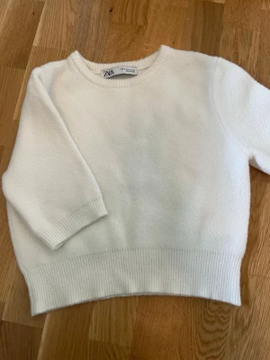 Vit stickad tröja från ZARA - Mysig vit kortärmad stickad tröja från ZARA med rund halsringning och ribbade muddar vid ärmslut och nederkant. Enkel och stilren design som passar perfekt till många outfits. Materialet känns mjukt och bekvämt mot huden. Med väldigt bra skick.