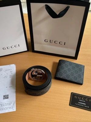 Svart GG-mönstrat bälte och bundle från Gucci - Snyggt svart bälte från Gucci med klassiskt GG-mönster och silverfärgat spänne. Bältet är gjort i skinn och har en stilren design som passar till många outfits. Perfekt accessoar för dig som gillar exklusiva detaljer.