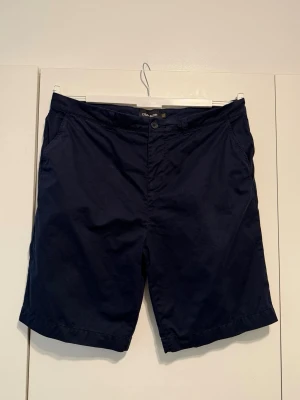 Mörkblå shorts från Lyle & Scott - Snygga mörkblå shorts från Lyle & Scott med klassisk passform. Shortsen har två sidofickor, två bakfickor med knapp och det ikoniska gula logomärket broderat ovanför ena bakfickan. Tillverkade i bomull för en skön känsla.
