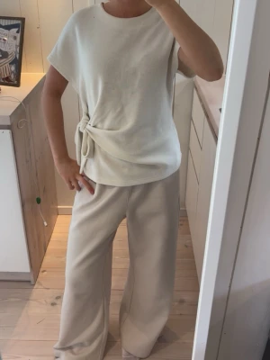 Beige loungewear-set med knytning - Mysigt loungewear-set i beige med kortärmad topp och knytning i midjan samt vida byxor. Perfekt för chill dagar hemma. Mjukt och bekvämt material med avslappnad passform.