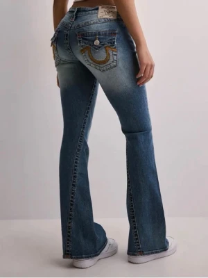 Blå bootcut jeans från True Religion modell joey - Säljer ett par blå bootcut jeans från True Religion med snygga kontrastsömmar. Jeansen har klassiska fem fickor, stora knappar bak och det ikoniska broderiet på bakfickorna. Tillverkade i denim med lätt stretch för skön passform. Jättebra skick lite problem med gylfen men går att fixa enkelt!