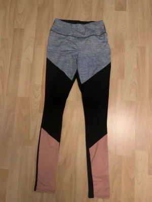 Färgglada sportleggings Beloved Woman - Sportiga leggings från Beloved Woman i storlek XS. De har en snygg färgblock-design med grått upptill, svarta partier i mitten och dammrosa nedtill. Stretchigt material som sitter tajt och bekvämt, perfekt för träning eller gym.