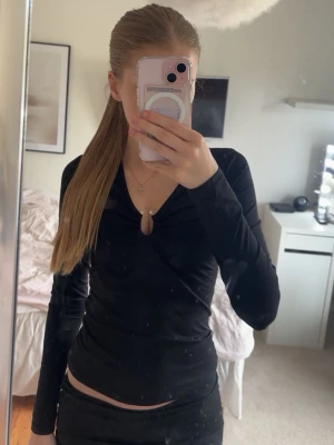 Svart långärmad omlottopp - Snygg svart långärmad topp med omlottdetalj och liten v-ringning framtill. Toppens material är stretchigt och sitter tight mot kroppen, perfekt för en trendig look.