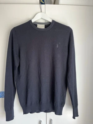 Mörkblå stickad tröja från Bruun & Stengade - Klassisk mörkblå tröja från Bruun & Stengade med rund halsringning och diskret logga på bröstet. Tröjan har ribbade muddar vid ärmslut och nederkant. Perfekt för en stilren och enkel look. Väldigt bra skick, använd sparsamt. Hör av er vid frågor eller funderingar 