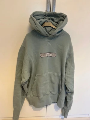 Grön hoodie från EYTIS - Snygg grön hoodie från EYTIS med broderad logga på bröstet. Hoodien har stor huva, magficka och ribbade muddar vid ärmslut och nederkant. Perfekt för en chill och avslappnad stil. Tillverkad i mjukt bomullsmaterial.