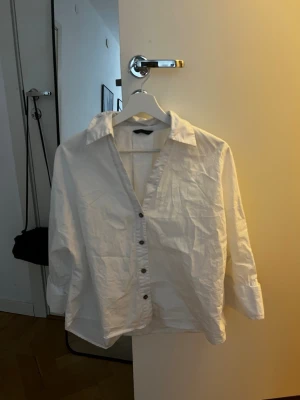 Vit klassisk skjorta med knappar - Vit skjorta med klassisk krage och knappar framtill. Skjortan har en avslappnad passform, perfekt för en stilren look. Tillverkad i bomull och passar till många olika outfits.