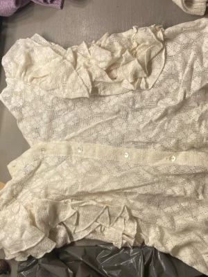Vit spetsblus med puffärmar - Söt vit blus i spetsmaterial med blommigt mönster och puffiga korta ärmar. Blusen har knappar bak och volangdetaljer vid axlarna. Perfekt för dig som gillar romantisk och trendig stil.