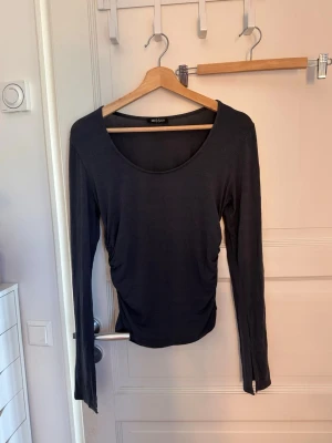 Mörkgrå långärmad topp från Missäy - Mörkgrå långärmad topp från Missäy med rund halsringning och snygga rynkade detaljer längs sidorna. Tunn och mjuk i materialet, perfekt att styla med jeans eller kjol för en clean look.