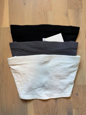 3-pack tubtoppar i svart, grå och vit - Tre stilrena tubtoppar i svart, grå och vit. Perfekta att matcha med olika outfits. Mjukt material och enkel design utan axelband för en clean look.