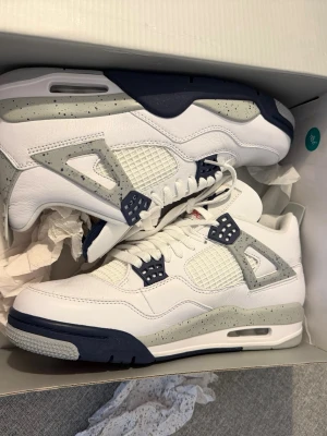 Air Jordan 4 White Oreo sneakers - Snygga Air Jordan 4 White Oreo sneakers i vitt läder med grå och mörkblå detaljer. Skorna har meshpaneler, speckled gråa inslag och klassisk AJ4-silhuett. Perfekta för dig som gillar streetwear och vill sticka ut med en ikonisk modell.
