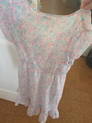 Blommig klänning med pastellfärger - Söt kortklänning med blommigt mönster i ljusrosa och ljusblå toner. Klänningen har volangdetaljer nertill och är tillverkad i ett lätt och luftigt material,. Den har korta ärmar och en bekväm passform med resår i midjan. Storleken är 146🩵 använd endast 1 gång (skolavslutning) Första bilden är baksidan på klänningen