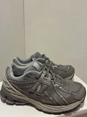 Grå New Balance 2002R sneakers - Snygga grå New Balance 2002R sneakers med mesh och syntetpaneler. Skorna har en chunky sula och reflekterande detaljer längs sidorna. Klassisk N-logga på sidan och skön vadderad insida. Perfekta för dig som gillar streetwear och sportig stil.