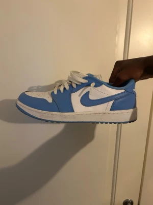 Nike Air Jordan 1 Low UNC blå/vit - Snygga Nike Air Jordan 1 Low i färgen UNC med blå och vita paneler. Skorna har klassisk låg siluett, vit tåbox och blå swoosh. Tillverkade i läder med vita skosnören och blå yttersula. Perfekta för dig som gillar streetwear och vill sticka ut.