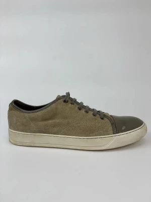 Beige Lanvin sneakers med lackad tå - Sneakers i beige mocka med grå snörning och en glansig, lackad tå i mörkgrått. Vit sula med diskret svart rand runt om. Snygg och stilren modell som passar till det mesta. Perfekt för dig som gillar en clean look med en twist.
