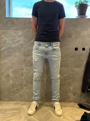 Ljusblå slim jeans med slitningar - Säljer ett par ljusblå slim fit jeans med slitna detaljer på knäna. Jeansen har klassisk femficksdesign och låg midja. Perfekta för en avslappnad och trendig look.