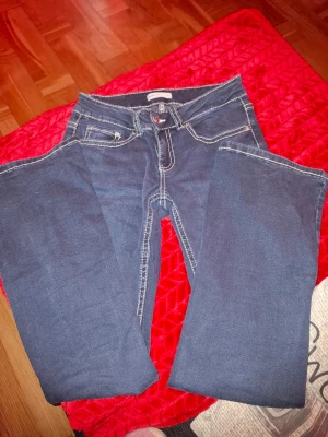 Mörkblå jeans med kontrastsömmar - Snygga mörkblå jeans med raka ben och tydliga vita kontrastsömmar. Klassisk femficksmodell med knappstängning och dekorativ bakficka. Perfekta för en avslappnad och trendig look.