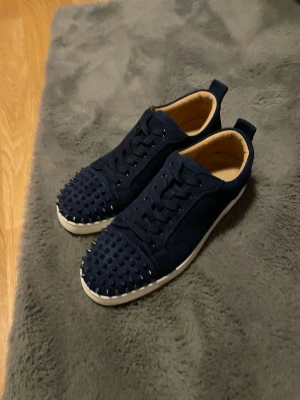Mörkblå sneakers med nitar - Unika mörkblå sneakers med coola nitar över tån och ovandelen. Skorna har en vit sula och är tillverkade i mockaliknande material. De har klassisk snörning och en låg profil som ger en modern vibe.🕶️kom DM