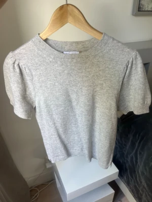 Ljusgrå puffärm kashmir tröja - Säljer en ljusgrå kashmir tröja med puffärmar och rund hals. Tröjan har korta ärmar och ribbade muddar vid hals och ärmslut. Perfekt för dig som gillar en enkel men trendig look.