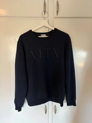 Mörkblå sweatshirt från Valentino - Snygg mörkblå sweatshirt från Valentino med VLTN-brodyr på bröstet. Klassisk rund halsringning och ribbade muddar vid ärmslut och nederkant. Perfekt för en stilren och avslappnad look.