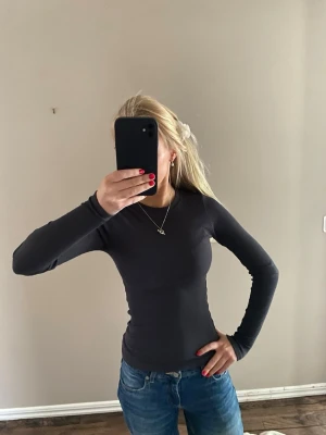 Svart långärmad ribbad topp - Snygg svart långärmad topp med tight passform och ribbad struktur. Perfekt basplagg som är enkel att styla till olika outfits. Mjuk och stretchig känsla.