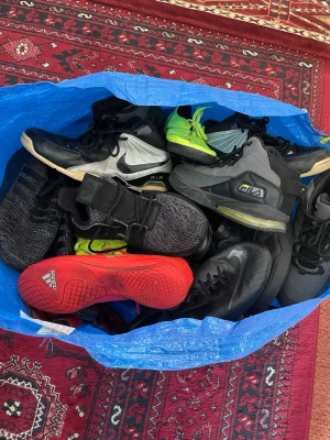 Mix av skor - Stor blå IKEA-kasse fylld med sneakers från Nike, Fila och Adidas och massa andra märken och skor. Skorna är i olika färger som svart, grå, röd och neon, med både klassiska och sportiga designer. Flera modeller har höga skaft och tydliga loggor. Perfekt för dig som gillar streetwear och sportig stil.