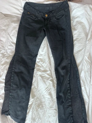 Omsydda svarta boot-cut jeans med blå sömm  - Snygga svarta bootcut jeans med dragkedjor på bakfickorna och dekorativa sömmar längs benen. Jeansen har låg midja och klassisk femficksdesign. Perfekta för dig som gillar en lite edgy stil och vill sticka ut med detaljer. Jag är 180 och jeansen passar mig i längden. Midja 30in och längd 32-34 in.