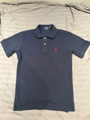 Marinblå pikétröja från Polo Ralph Lauren - Säljer marinblå pikétröja från Polo Ralph Lauren. Har använt ett litet tag nu och har inga skador eller defekter och använder inte mer längre, väldigt stilig och skön