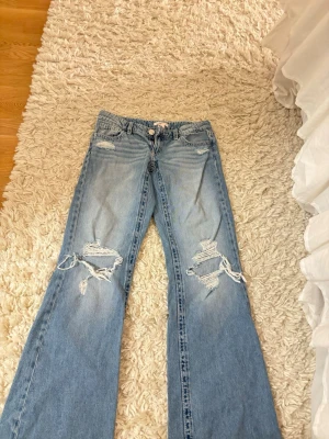 Ljusblå baggy jeans - Säljer ett par ljusblå baggy jeans med stora slitningar och hål på båda knäna. Dom perfekta jeansen! Storleken är XS 14+.
