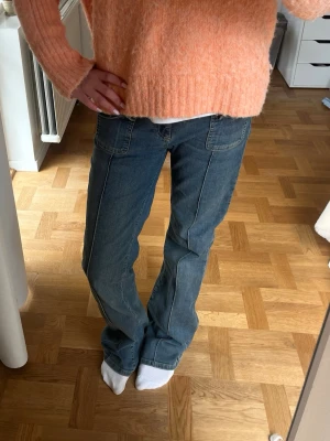 Blå bootcut jeans med fickor fram - Snygga blå bootcut jeans med markerade sömmar och två stora fickor framtill. Jeansen har hög midja och klassisk dragkedja med knapp. Perfekta för en avslappnad och trendig look.