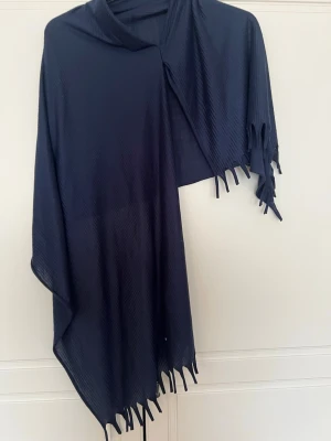 Mörkblå sjal med fransar instans hijab - Snygg mörkblå sjal i mjukt tyg med diskret struktur och fransar längs kanterna. Perfekt att svepa runt axlarna för en stilren look. Enkel att matcha med olika outfits och ger en cool touch till din stil.