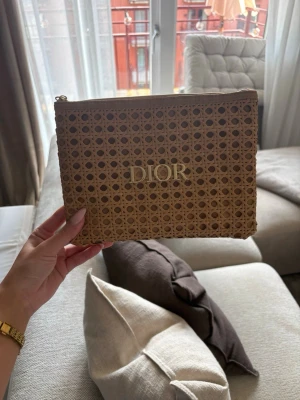 Beige kuvertväska från Dior - INTRESSEKOLL!!  Snygg beige kuvertväska från Dior med flätad rottinglook och guldfärgad logga framtill. Väskan har en rektangulär form och stängs med dragkedja upptill.            