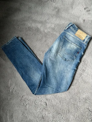 Ljusblå slim fit jeans från replay - Säljer ett par ljusblå slim fit jeans från replay med klassisk femficksdesign och snygga slitningar. Jeansen har en rak passform och är tillverkade i bomull med en skön stretch. 