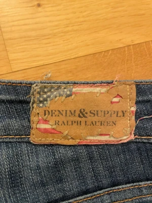 Blå jeans från Ralph Lauren - Snygga blå jeans från Denim & Supply Ralph Lauren med klassisk femficksdesign och slitna detaljer. Jeansen har en cool tvätt och är gjorda i denim med tydliga sömmar och knappgylf. Perfekta för en avslappnad och trendig stil. !pris kan diskuteras!