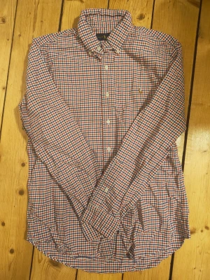 Rutig skjorta från Ralph Lauren - Klassisk långärmad skjorta från Ralph Lauren i rött, blått och vitt rutmönster. Skjortan har knappar framtill, button-down krage och den ikoniska broderade loggan på bröstet. Tillverkad i mjuk bomull för en bekväm känsla.